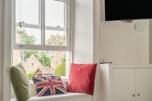 Ein Zimmer mit Fenster, einem roten Kissen, einem grünen Kissen und einem an der Wand befestigten Flachbildfernseher.