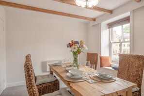 A dining area with a wooden table set for four, surrounded by wicker chairs, a vase of flowers, and a view of the outside through a large window. - 3 Bed in Allendale (oc-b45877) (Allendale Town)