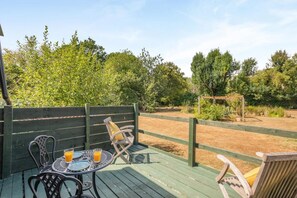 Un espace extérieur aménagé avec une table et des chaises, entouré d’une terrasse en bois et d’un jardin clos.