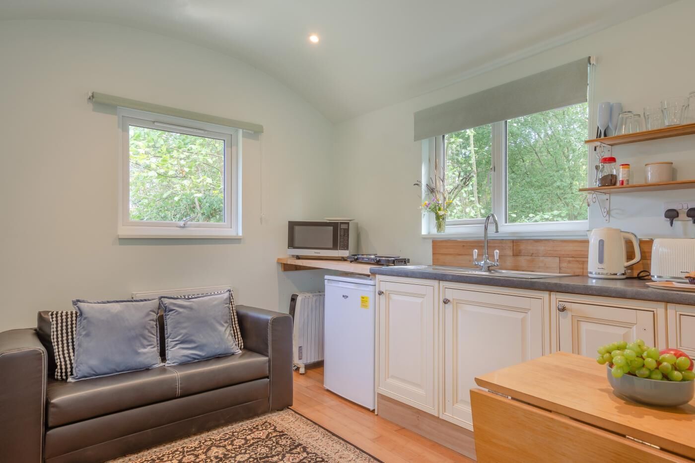 A compact kitchen with a microwave, kettle, and a bowl of fruit on the counter.