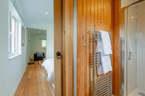 A hotel room with a wooden floor, a bed, a small bedside table, and a shower area with a towel rack. - 1 Bed in Laddingford (oc-s45858) (Laddingford)