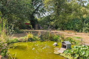 Ein Teich mit Seerosenblättern, umgeben von üppiger Vegetation und einer Holzkonstruktion.