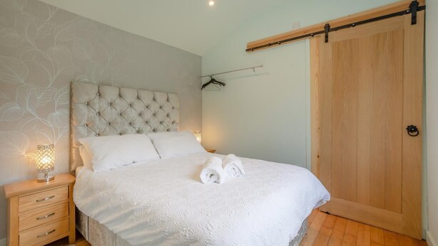 A bedroom with a tufted headboard, a wooden floor, a wooden wardrobe, and a bedside table with a lamp. - 1 Bed in Laddingford (oc-s45858) (Laddingford)