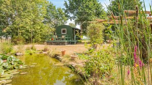A rustic cabin with a deck, surrounded by a pond, trees, and a wooden fence. - 1 Bed in Laddingford (oc-s45859) (Laddingford)