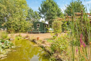 A rustic cabin with a deck, surrounded by a pond, trees, and a wooden fence. - 1 Bed in Laddingford (oc-s45859) (Laddingford)