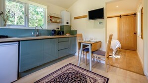 A compact kitchen with a built-in dishwasher, a dining area with a table and chairs, and a TV mounted on the wall. - 1 Bed in Laddingford (oc-s45859) (Laddingford)
