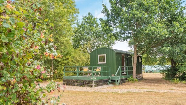 A green cabin with a deck, surrounded by trees and a gravel path. - 1 Bed in Laddingford (oc-s45859) (Laddingford)
