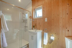 Ein Badezimmer mit Duschkabine aus Glas, einem weißen Waschbecken und Holzvertäfelung.