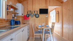 A compact kitchen with wooden walls, a dining area with a table and chairs, and a TV mounted on the wall. - 1 Bed in Laddingford (oc-s45860) (Laddingford)