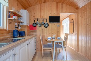 Eine kompakte Küche mit Holzwänden, ein Essbereich mit Tisch und Stühlen sowie ein an der Wand befestigter Fernseher.