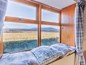 A room with a large window offering a view of a field and mountains. There is a bench with a plaid cushion. - 4 Bed in Boat Of Garten (oc-78920) (Boat of Garten)