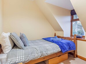 A single bed with a checkered bedspread and pillows, a wooden headboard, a small desk with a chair, and a window with a view of trees. - 4 Bed in Boat Of Garten (oc-78920) (Boat of Garten)