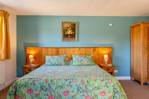 A bedroom with a floral bedspread, wooden headboard, two bedside tables with lamps, and a wooden wardrobe. - 1 Bed in Boys Hill (oc-b45932) (Boys Hill)