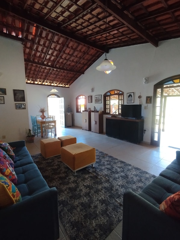A spacious living area with a high ceiling, a television, and a dining area with chairs and a table.