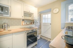 A kitchen with white cabinets, a stone wall, a clock, and a window. - 1 Bed in Grasmere (oc-lr250) (Grasmere)