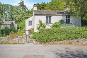 A white house with a stone wall and a wooden gate, surrounded by greenery. - 1 Bed in Grasmere (oc-lr250) (Grasmere)