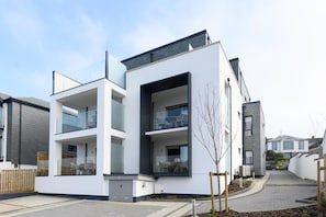 Un immeuble résidentiel moderne à deux étages, doté d’un toit plat, de grandes fenêtres et d’une porte de garage bien visible.