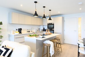 A modern kitchen with white cabinetry, a central island with stools, and pendant lighting. - 2 Bed in Falmouth (oc-b669263) (Flushing)