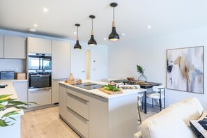 A modern kitchen with a central island, pendant lighting, and a dining area with a white sofa. - 2 Bed in Falmouth (oc-b669263) (Flushing)