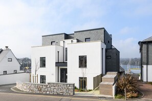 Un edificio residencial moderno con techo plano, varias ventanas y un camino de piedra que lleva a la entrada.