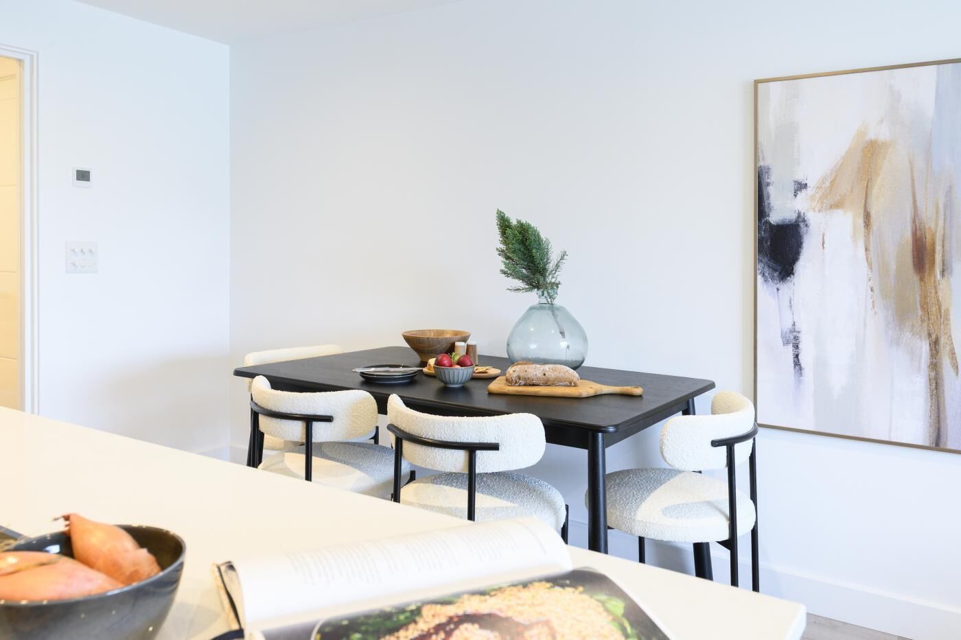 A dining area with a dark table, white chairs, and a vase with greenery.