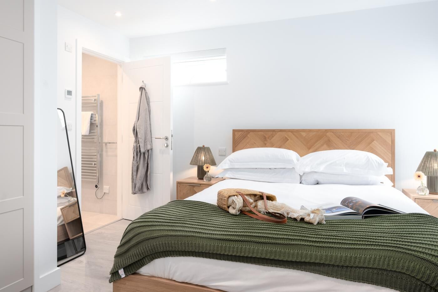 Une chambre à coucher moderne avec une tête de lit en bois, une couverture verte en tricot et un livre sur le lit.