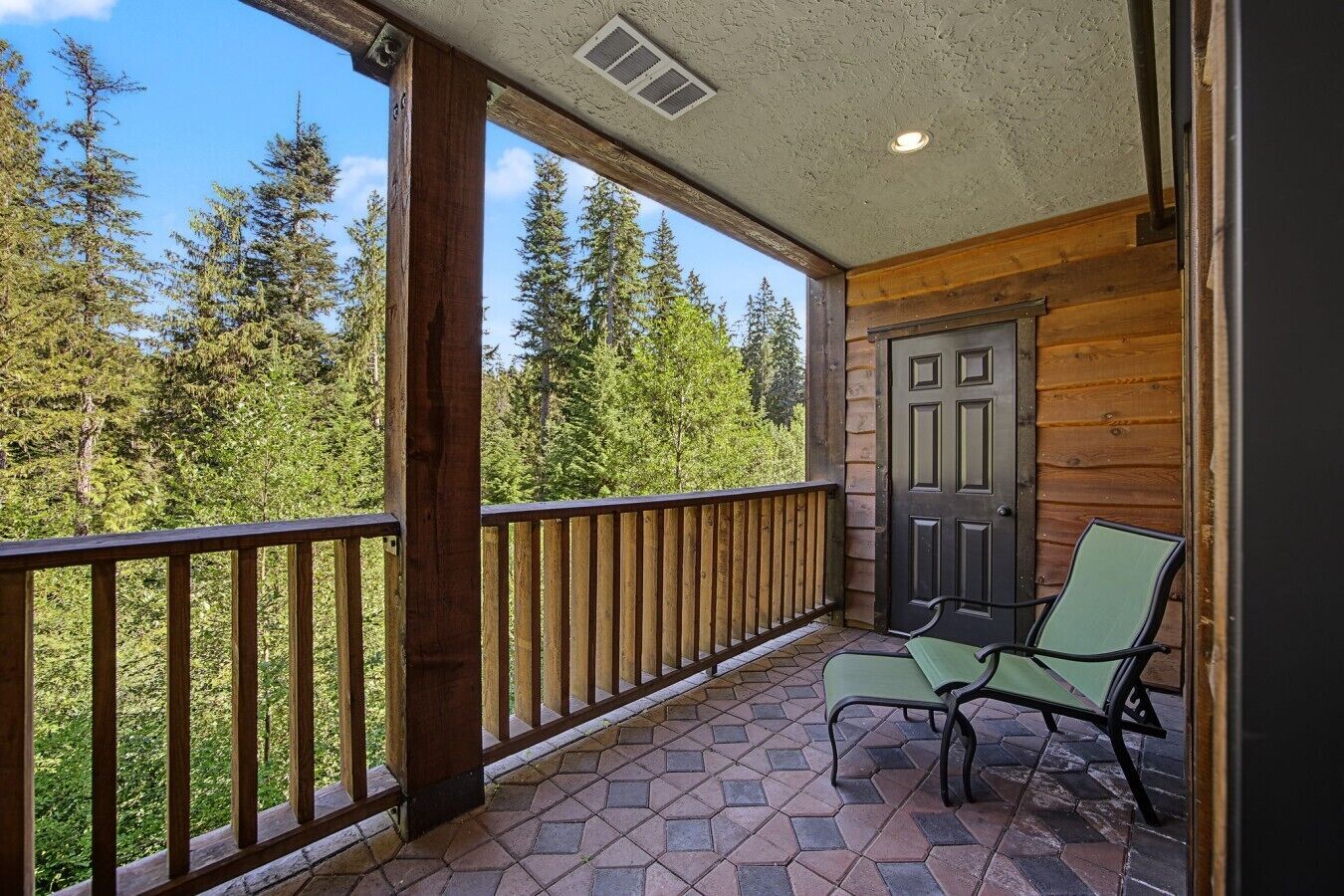 Un balcon en bois donnant sur des arbres, avec une porte et deux chaises.