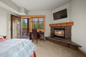 A bedroom with a bed, a desk, a chair, a fireplace, and a TV mounted on the wall.