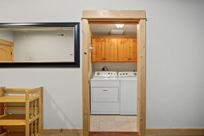 A compact laundry room with wooden cabinets and a washing machine. - Trillium Lake Condo 302 at South Grand Lodge | Tree-Lined Balcony Views (Government Camp)