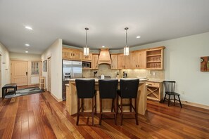 A modern kitchen with wooden cabinets, a stainless steel refrigerator, and a bar area with stools. - Trillium Lake Condo 302 at South Grand Lodge | Tree-Lined Balcony Views (Government Camp)