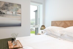 Un dormitorio con cama, mesita de noche, lámpara, ventana y un cuadro en la pared.