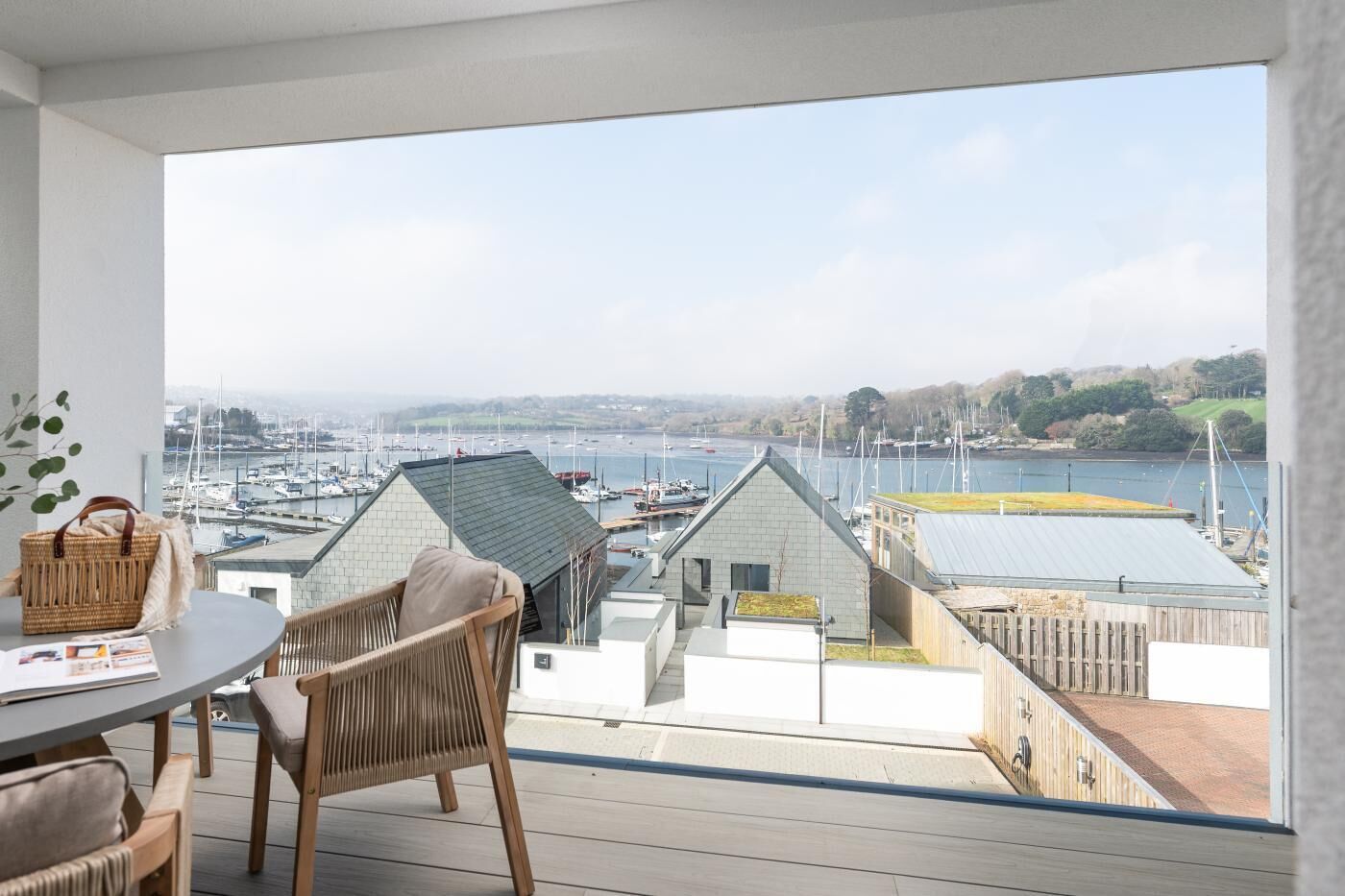 A balcony with a view of a marina, wicker furniture, and a table with a basket.