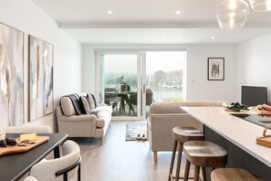 A modern kitchen with a central island, a dining area with a glass table, and a living room with a sofa and chairs. - 2 Bed in Falmouth (oc-b669265) (Flushing)