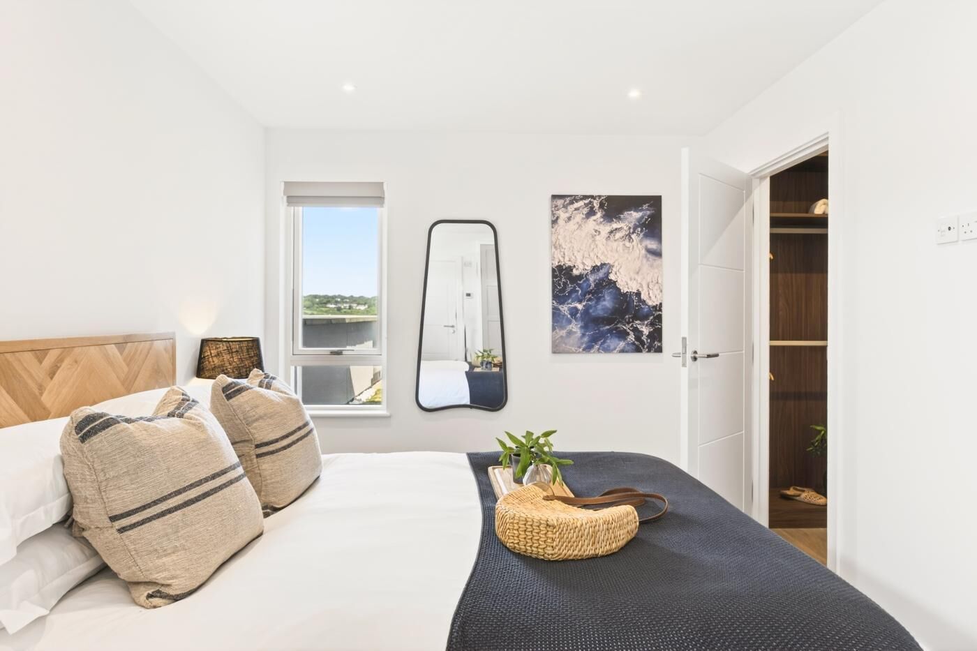 A bedroom with a bed, a bedside table, a mirror, a window, and a wardrobe.