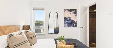 A bedroom with a bed, a bedside table, a mirror, a window, and a wardrobe.