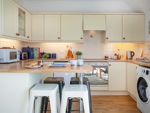 Eine kompakte Küche mit Mikrowelle, Toaster und Kaffeemaschine. Es gibt Hocker und eine Waschmaschine.