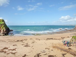 Ein Strand mit einem felsigen Felsen links und einer Gruppe von Menschen rechts.