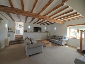 A spacious living room with exposed wooden beams, a grey sofa, a coffee table, and a television. - 4 Bed in Colyton (oc-b45892) (Colyton)