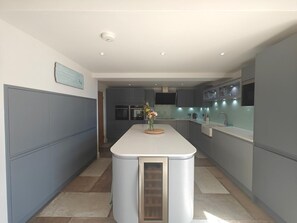 A modern kitchen with a central island, grey cabinetry, and a flat-screen TV mounted above the island. - 4 Bed in Colyton (oc-b45892) (Colyton)
