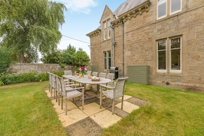 A stone building with a patio table and chairs, surrounded by a well-maintained lawn and trees. - 5 Bed in Cornhill-on-Tweed (oc-s45856) (Cornhill-on-Tweed)