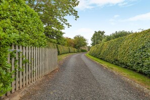 Ein gepflegter Schotterweg, gesäumt von ordentlich geschnittenen Hecken und einem Holzzaun.