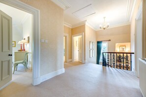 A spacious hallway with a carpeted floor, a staircase with a black railing, and a chandelier. - 5 Bed in Cornhill-on-Tweed (oc-s45856) (Cornhill-on-Tweed)
