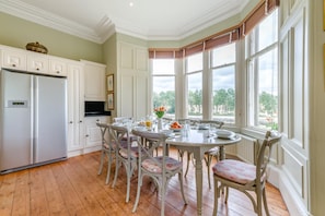 A dining area with a table set for four, surrounded by chairs, in a room with wooden flooring and large windows. - 5 Bed in Cornhill-on-Tweed (oc-s45856) (Cornhill-on-Tweed)
