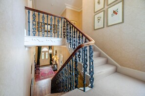 Eine imposante Treppe mit aufwendig gestalteten, blauen Balustraden und einem Holzgeländer, die zu einer Empfangshalle mit rotem Teppich und einer Tür führt.