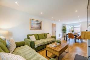 Uma sala de estar moderna com um sofá verde, uma mesa de centro de madeira e um espaço de jantar com mesa e cadeiras.