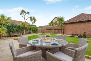 A circular outdoor dining area with wicker furniture and a glass table, surrounded by a brick building and a wooden fence. - 4 Bed in Seahouses (oc-h45933) (Seahouses)