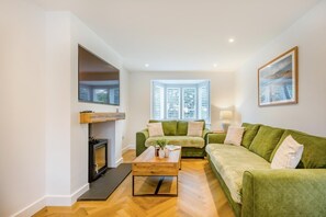 A living room with a fireplace, green sofas, a coffee table, and a large window with blinds. - 4 Bed in Seahouses (oc-h45933) (Seahouses)