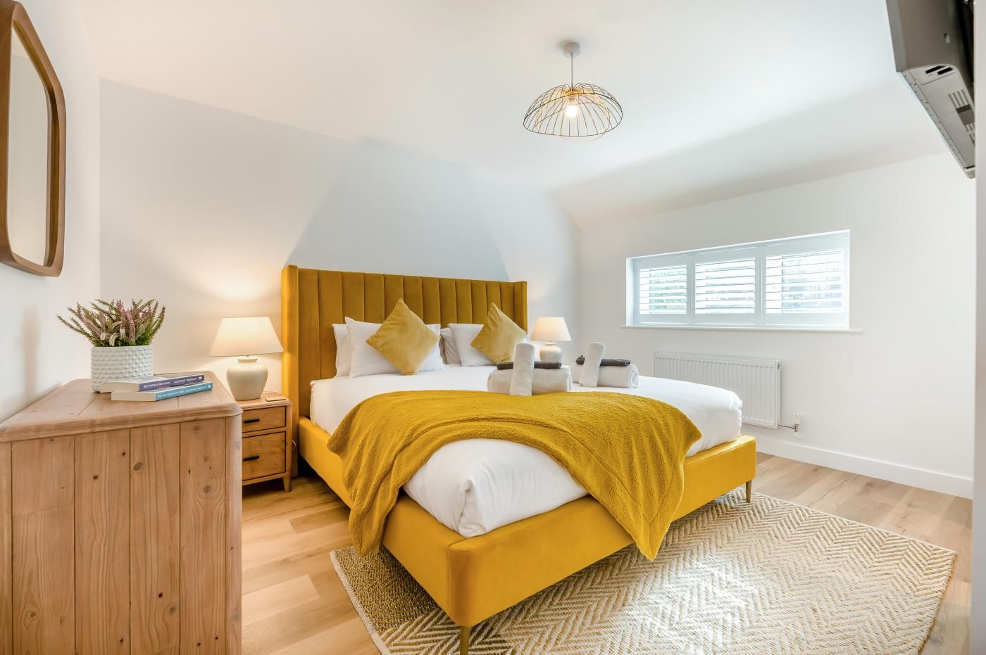 Een slaapkamer met een bed, nachtkastjes, een lamp, een raam en een plafondlamp.