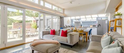 A spacious living area with a sofa set, a dining table, and a kitchen in the background.
