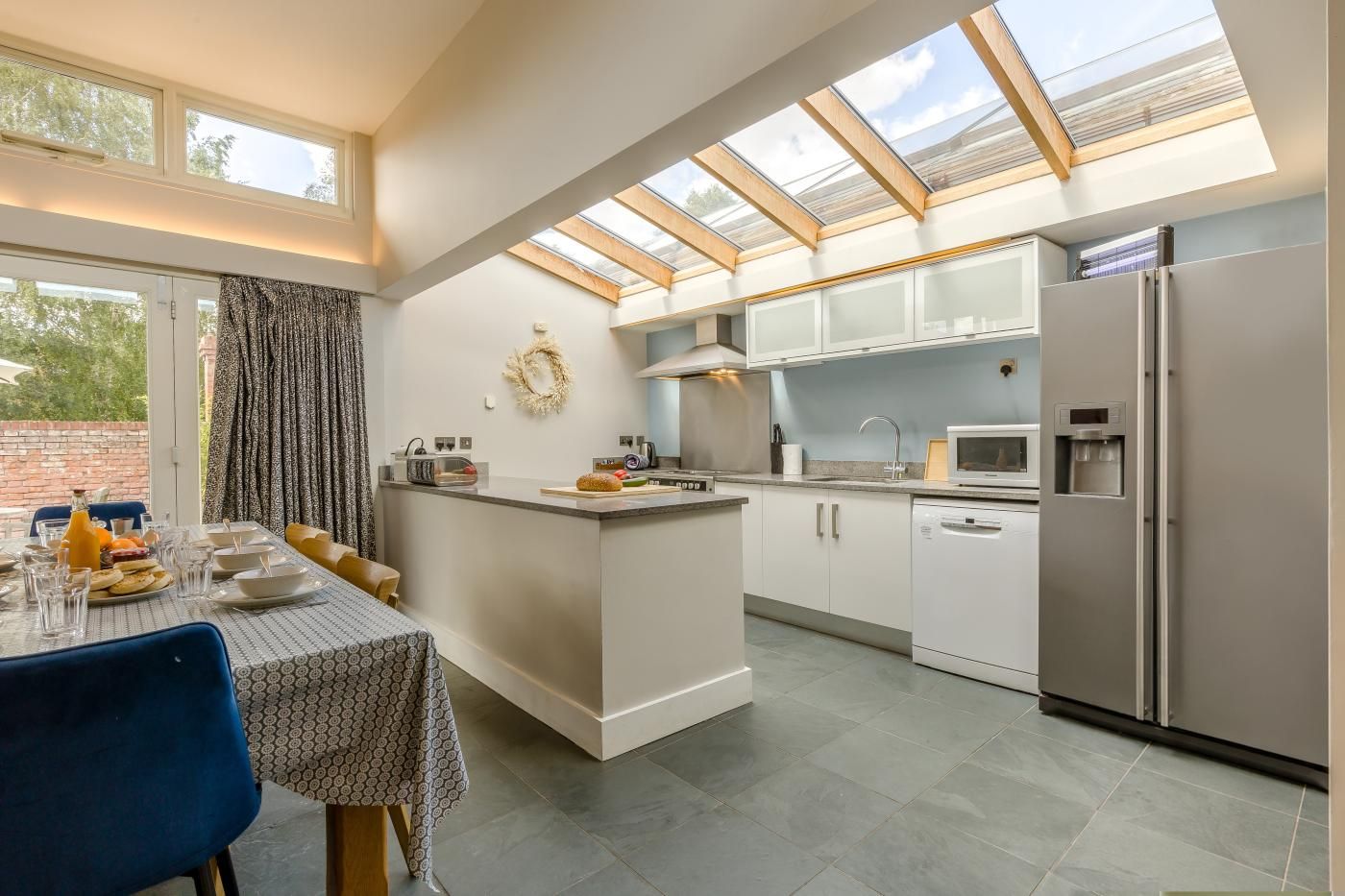 A modern kitchen with a central island, a dining area with a table set for two, and a large skylight above.